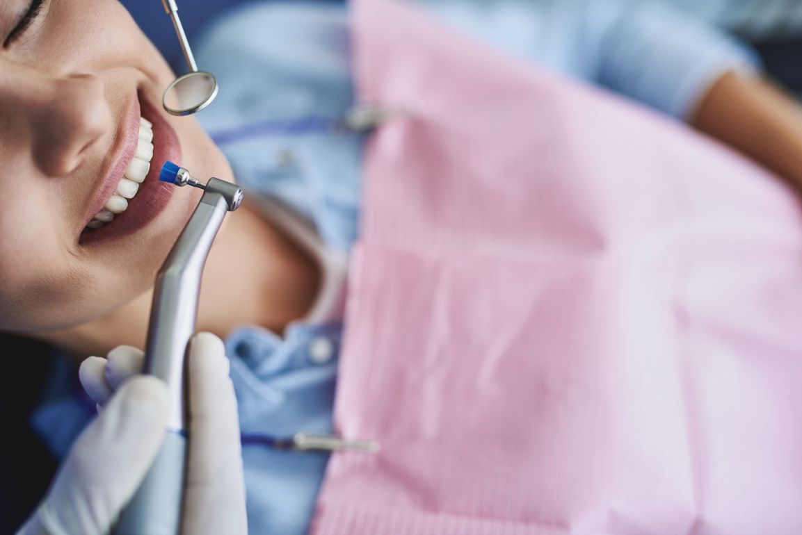 Patient recevant des soins dentaires. Dentiste utilisant des instruments pour examiner et nettoyer les dents ; champ opératoire rose.