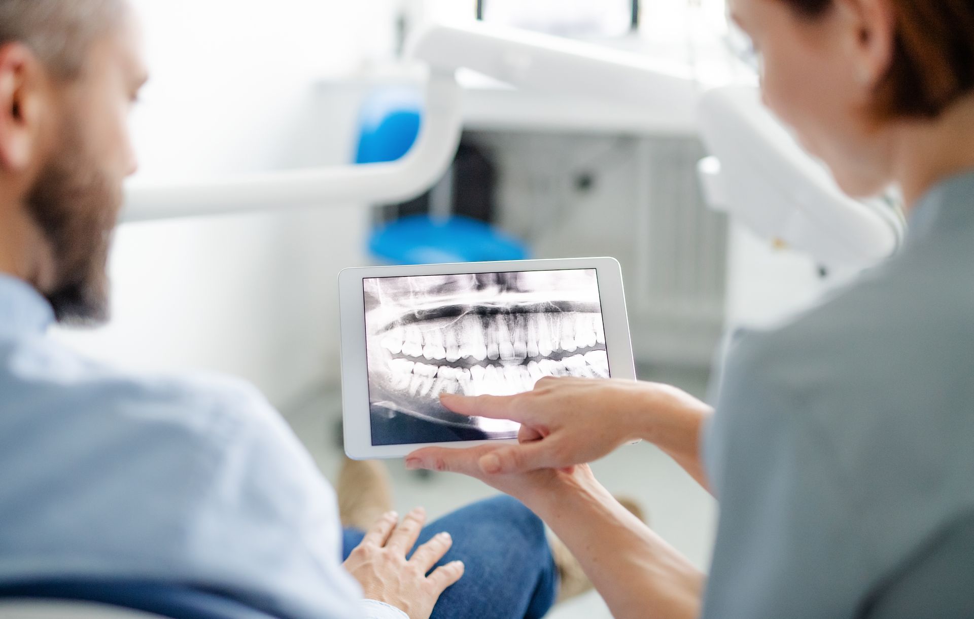 Un dentiste montre du doigt la radiographie dentaire d'un patient sur une tablette dans son cabinet.