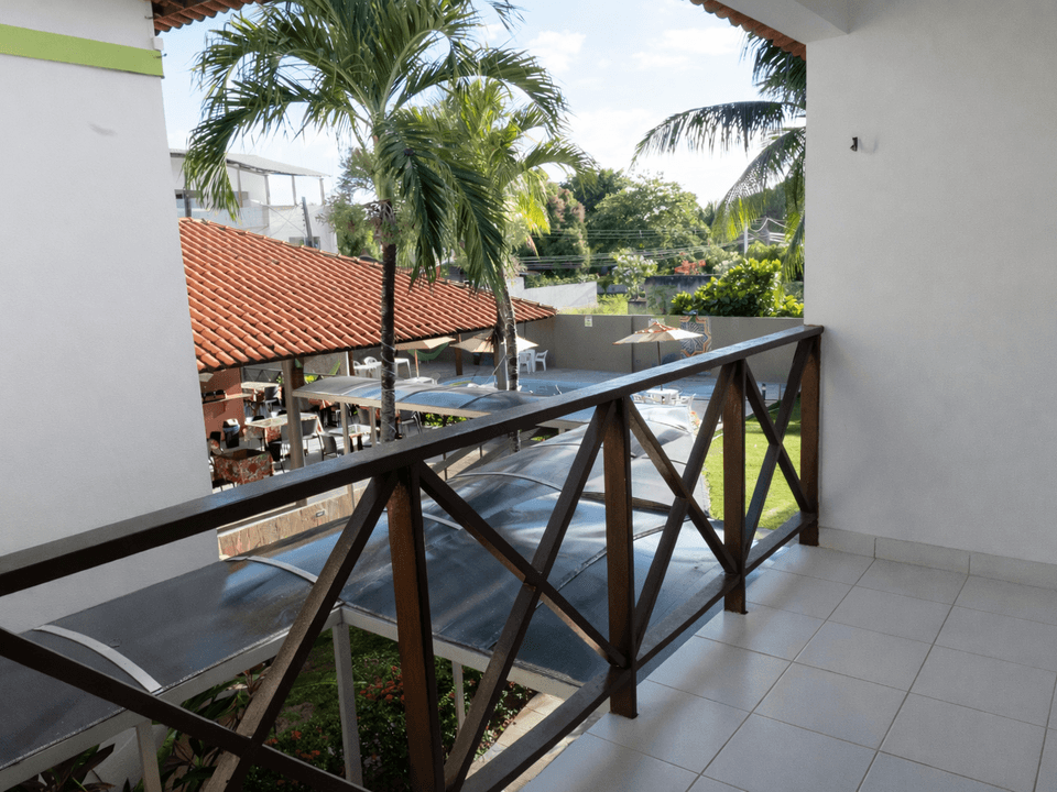 Varanda com corrimão de madeira com vista para um pátio com palmeiras e um restaurante.