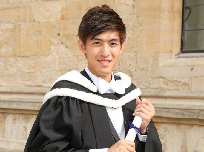 A young man in a graduation gown is holding a diploma