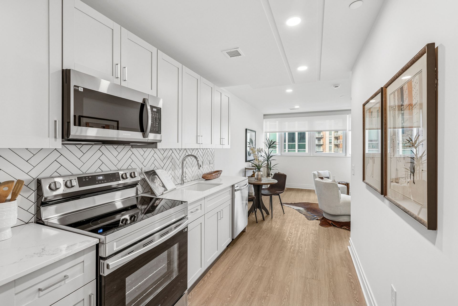 Modern white kitchen with stainless steel appliances, open to a living area with artwork.