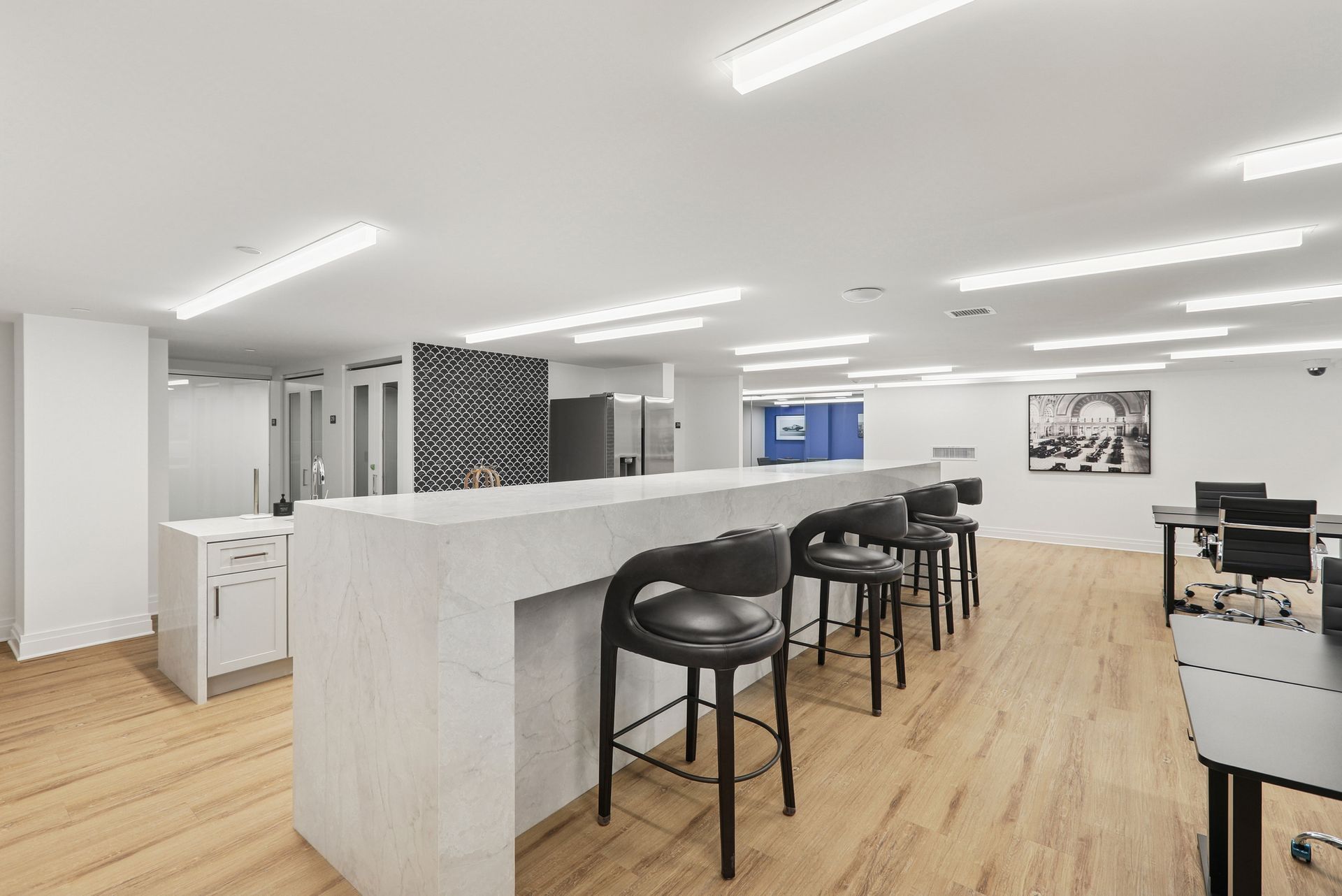 Modern office break room with bar seating, wooden floors, and workstation tables.