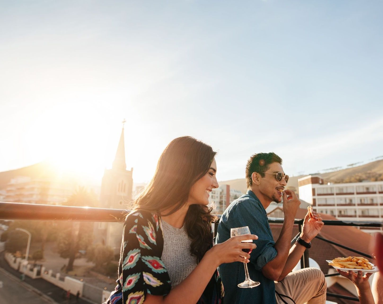 A group of people are sitting on a balcony drinking wine and eating pizza.
