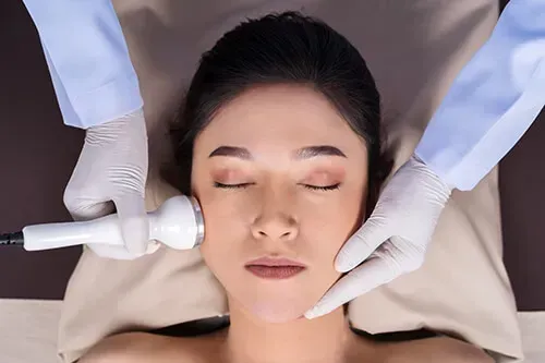 Woman receiving facial treatment; aesthetician using a device on her cheek.