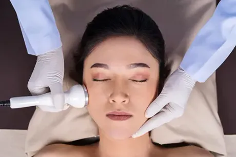 Woman receiving facial treatment; aesthetician using a device on her cheek.