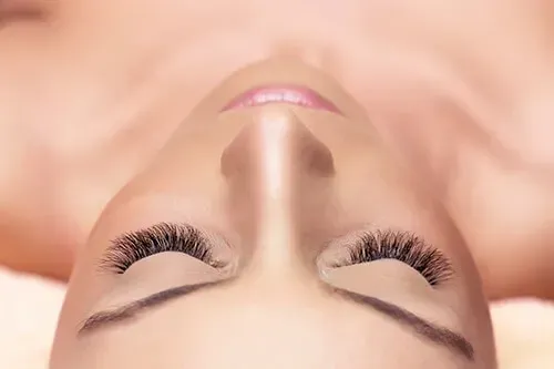 Woman with closed eyes, lush eyelashes, and light makeup, lying down.