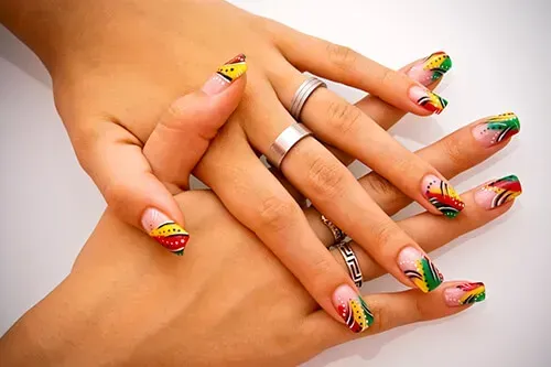 Hands with colorful nail art in red, yellow, and green, with silver rings.