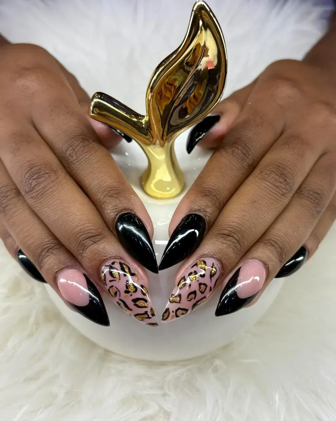 Hands with black stiletto nails, cheetah print accents. A gold decorative figure sits between them.