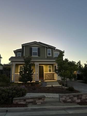 Two-story house with a lit porch at dusk and a landscaped front yard