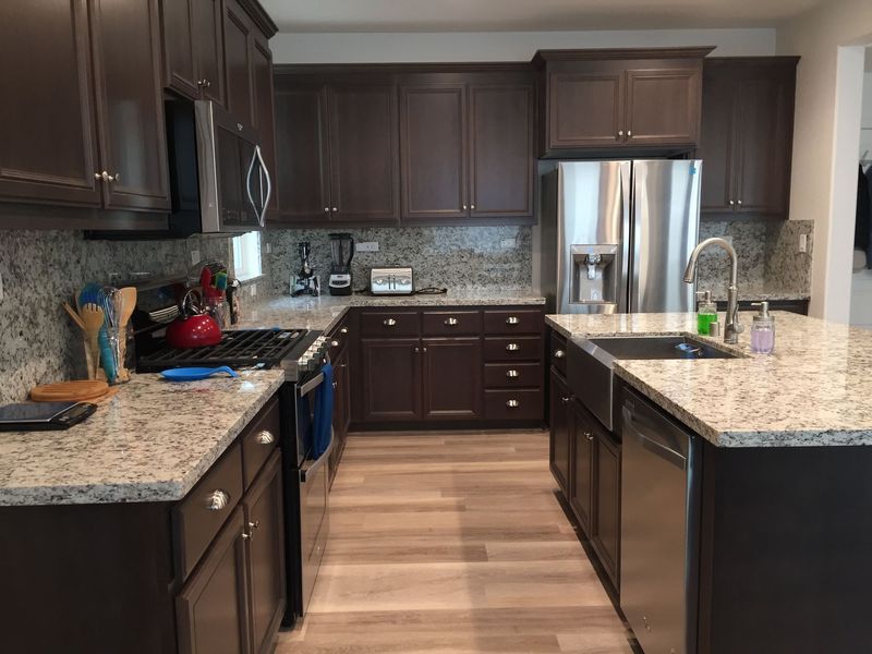 A modern kitchen featuring dark wood cabinets, light granite countertops, stainless steel appliances, and wood flooring.