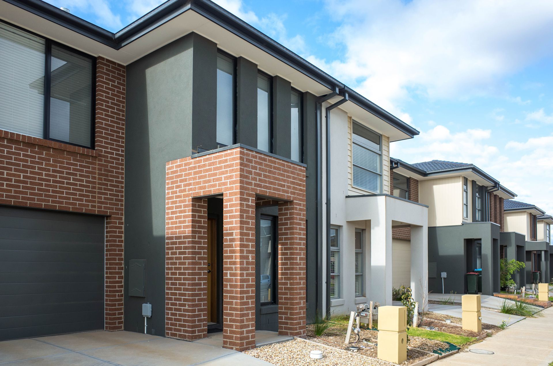 A row of modern two-story townhouses with brick and painted facades and attached garages on a sunny day.