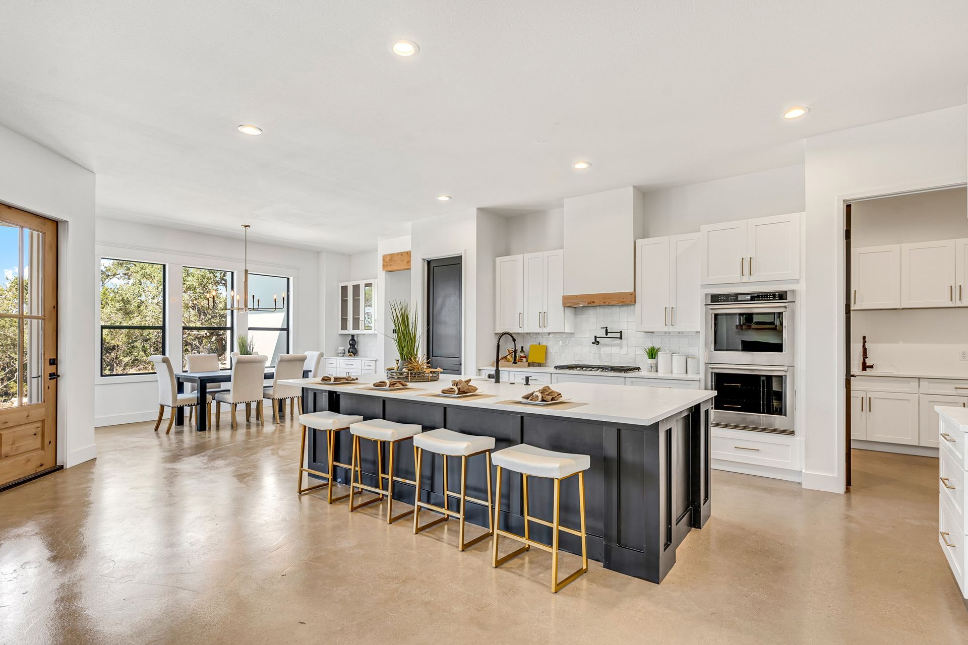 A bright, modern kitchen with white cabinets, a large dark blue island with four bar stools, and a dining area nearby.
