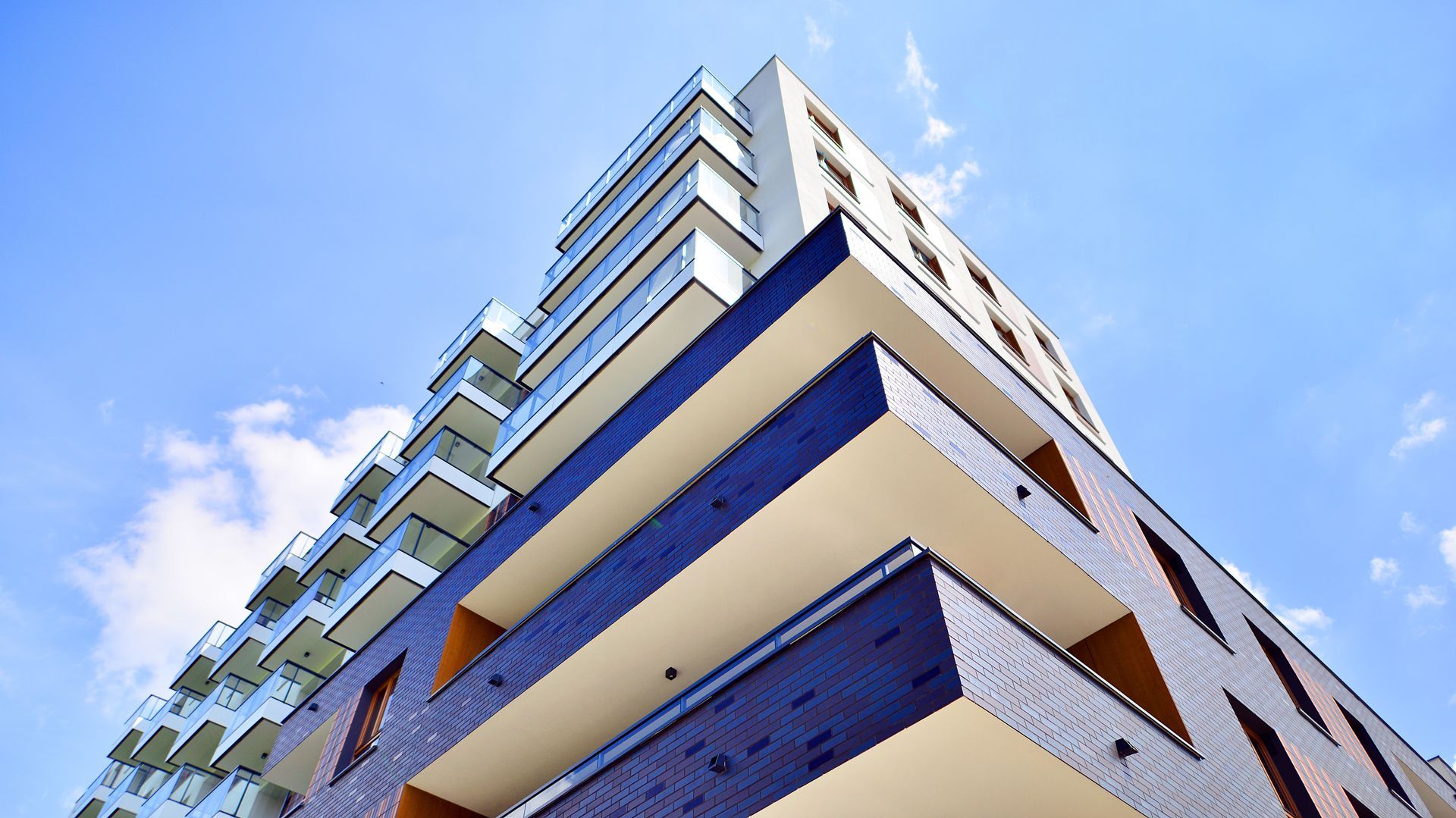 A low-angle view of a modern multi-story apartment building with dark blue brick facades and white balconies.