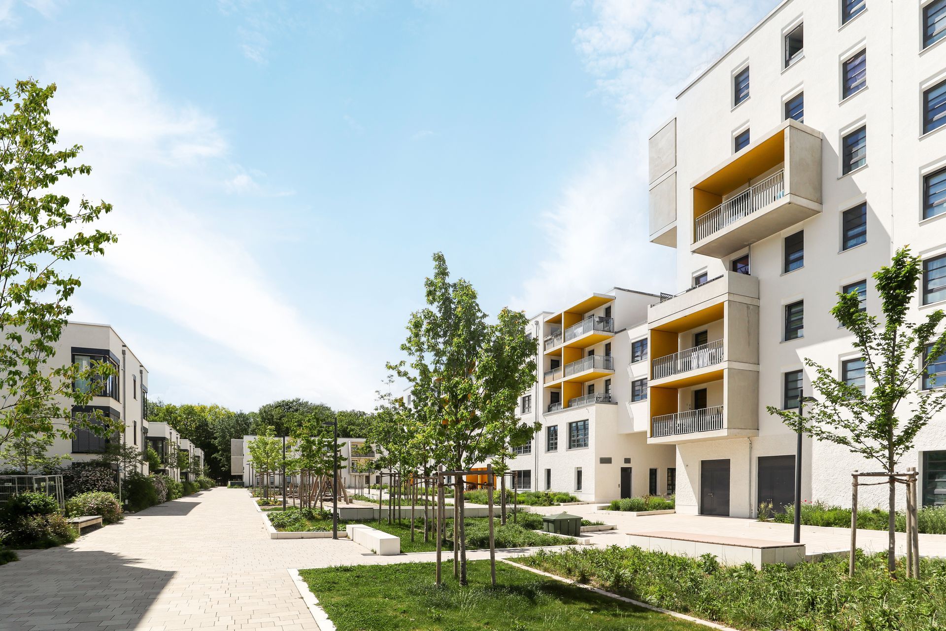 Modern apartment buildings with balconies beside a landscaped courtyard and walkway