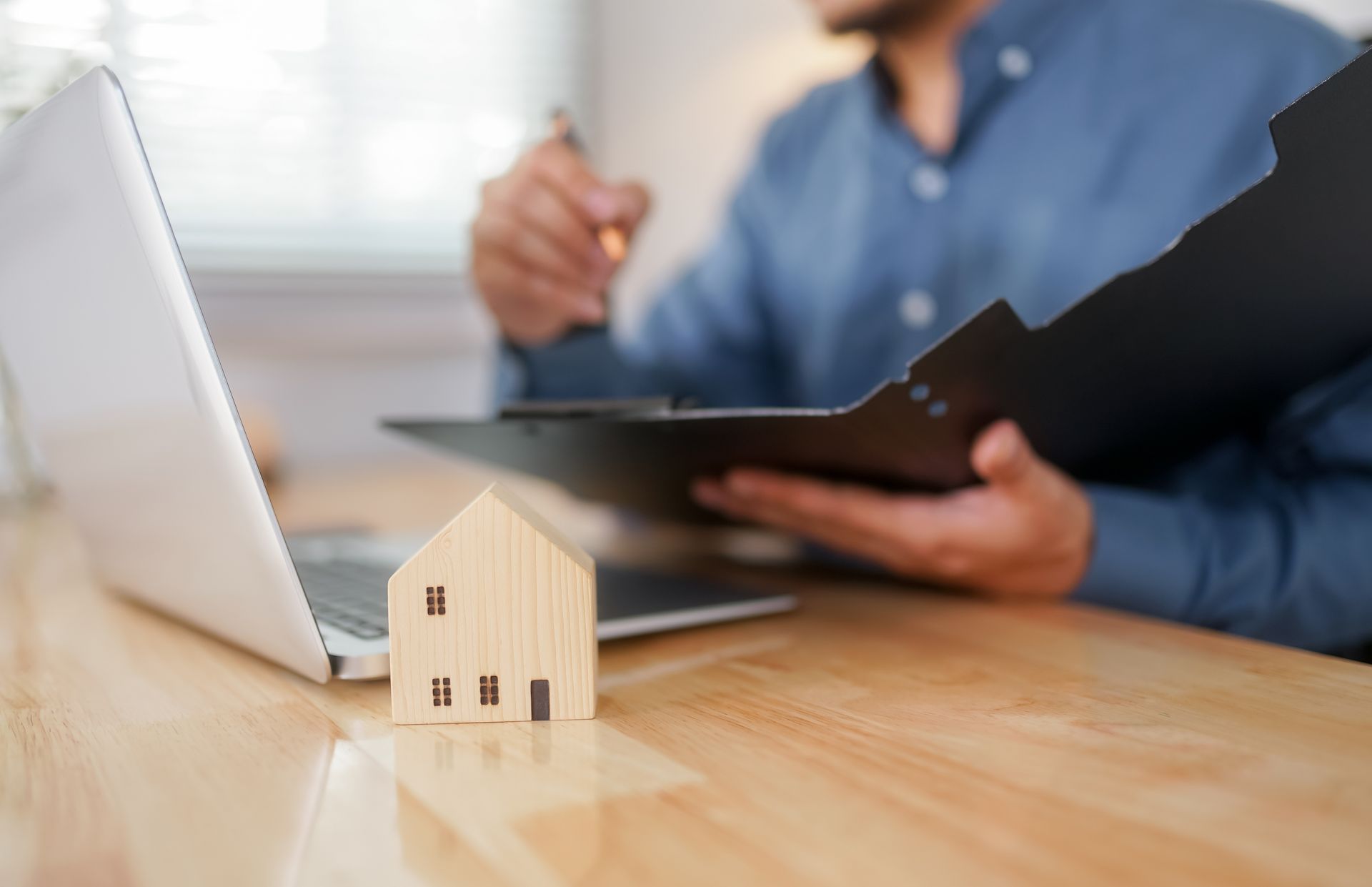 Small house model on a desk with a person holding a clipboard in the background