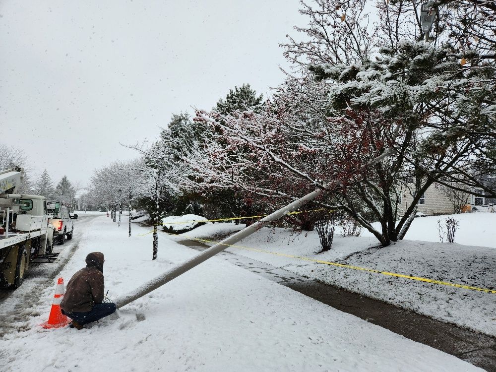A man is kneeling in the snow next to a fallen pole.