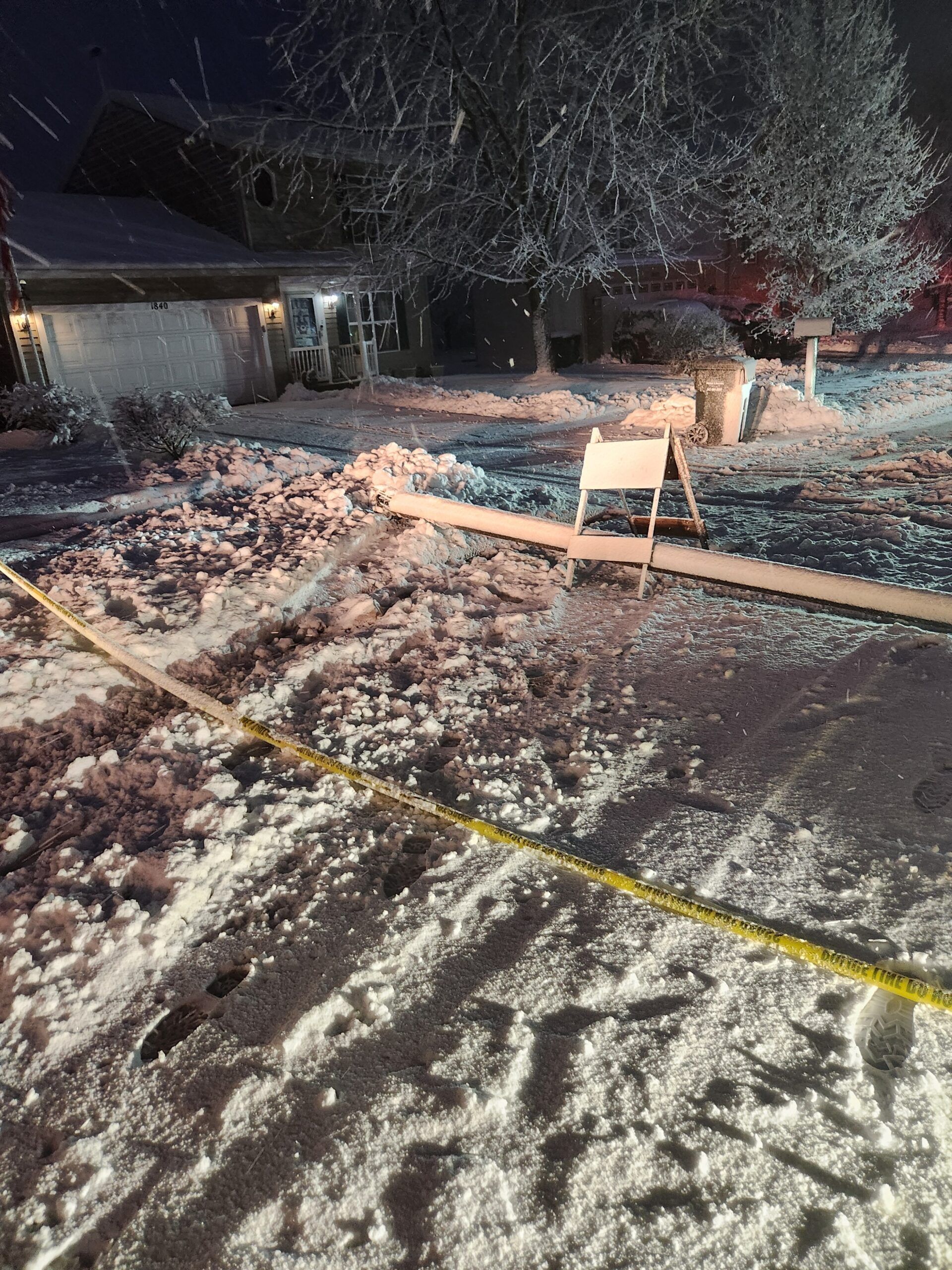 A snowy yard with a house in the background and a hose in the foreground.