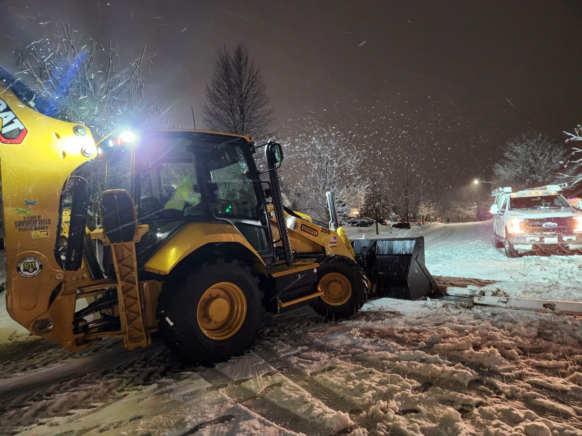 A yellow bulldozer is driving through the snow at night.