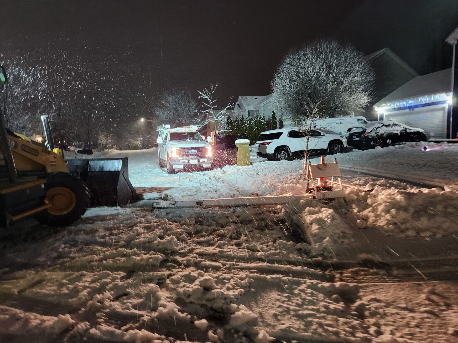 A snow plow is clearing snow from a driveway at night.