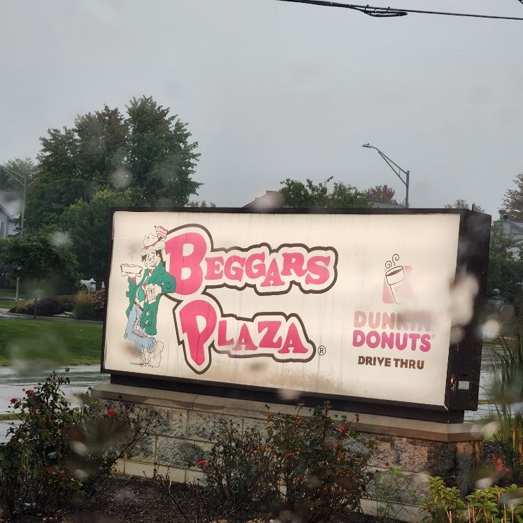 Sign for Beggars Plaza with a Dunkin' Donuts drive-thru in the rain.
