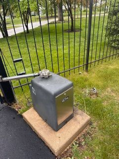 Black metal gate opener on concrete base in grassy yard. Black metal gate opener on concrete base in grassy yard.
