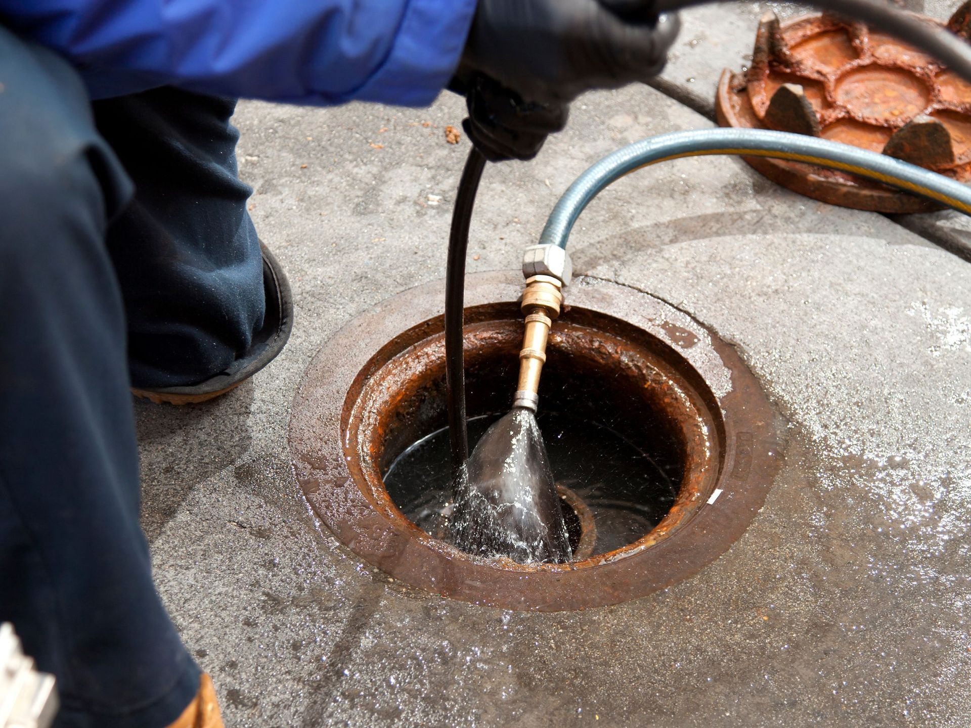 A person is cleaning a manhole cover with a hose.