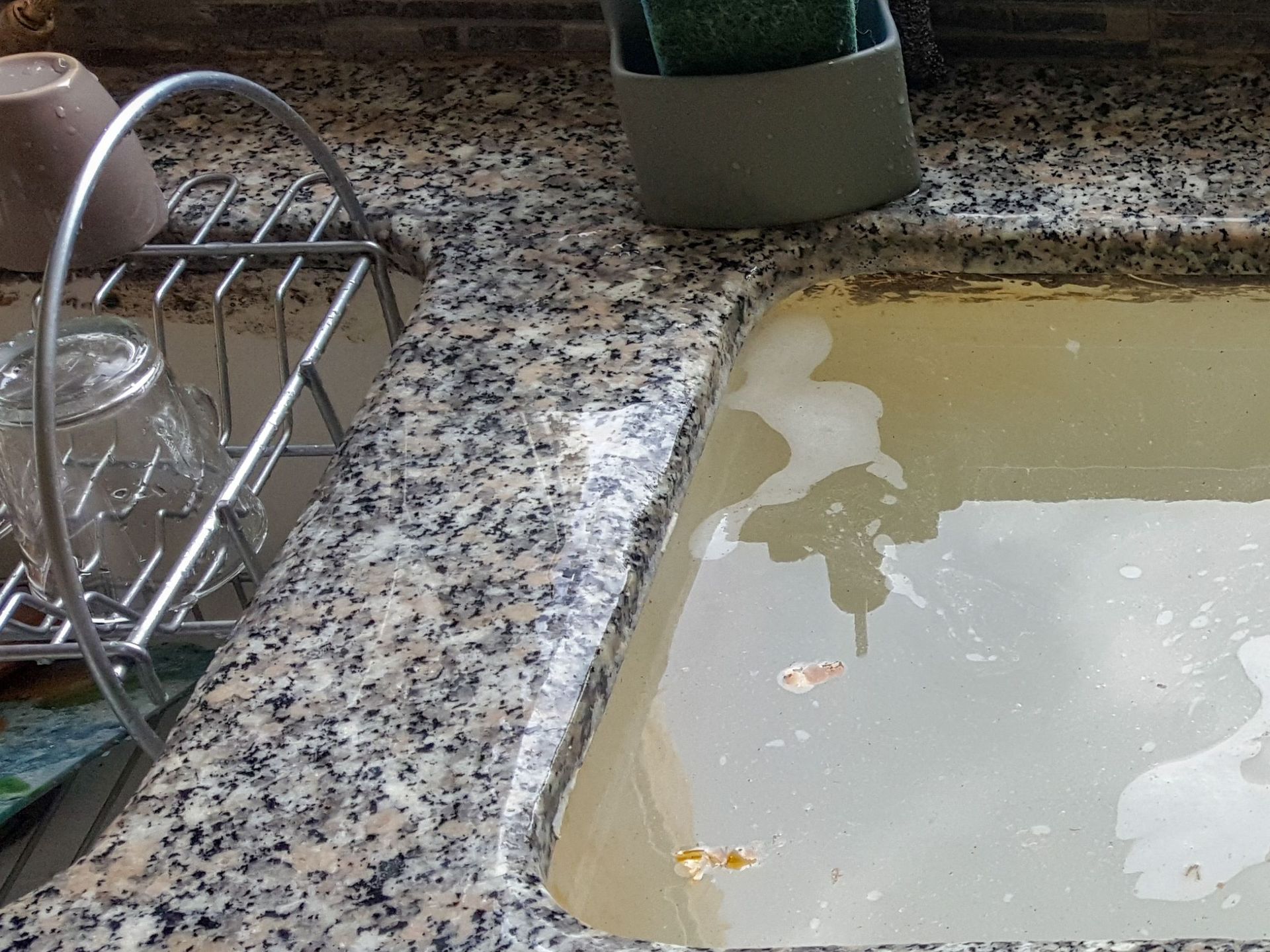 A sink with a sponge and a sponge holder next to it