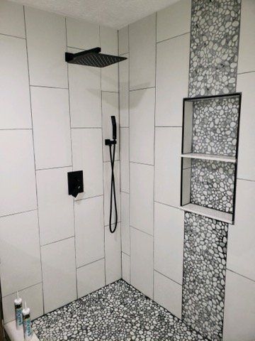 A shower with white tiles and a black shower head.