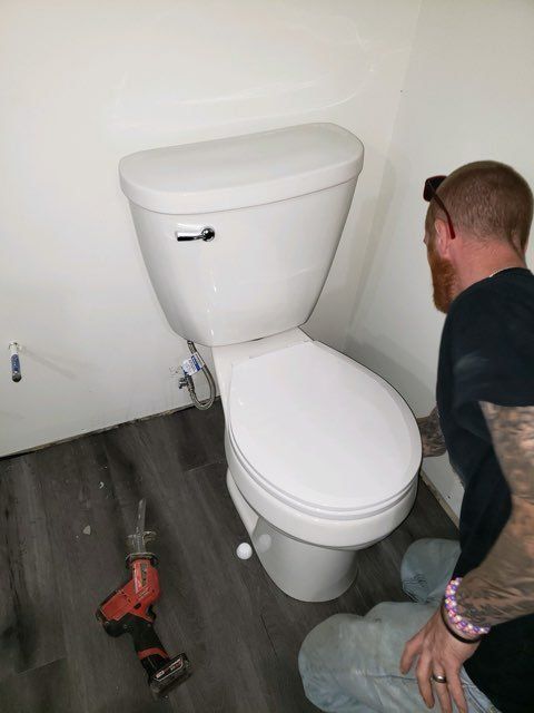 A man is kneeling next to a toilet in a bathroom.
