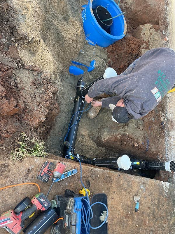 A Man Is Working On A Pipe In The Dirt — Pertzels Plumbing In Wagga Wagga, NSW