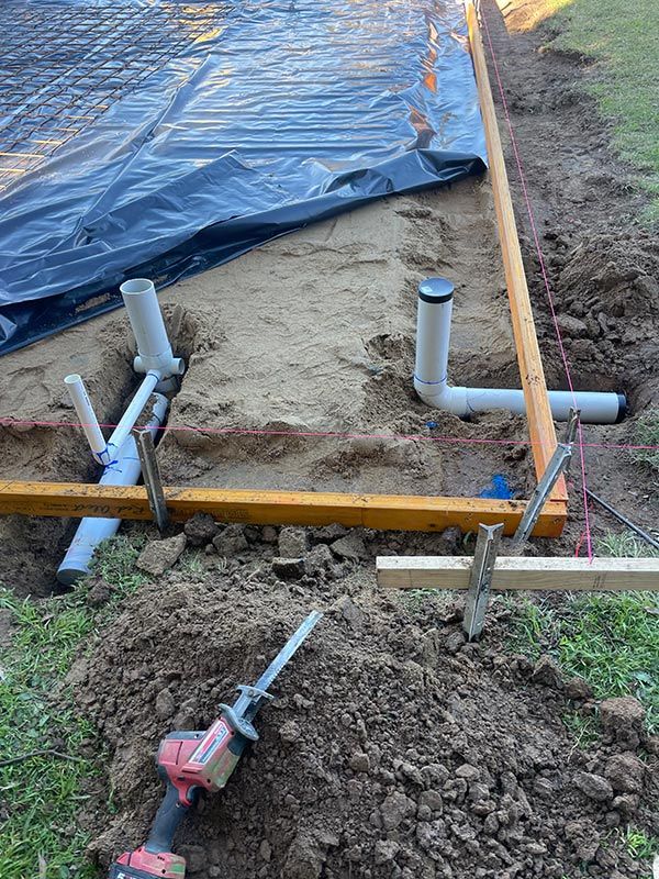 A Drill Is Sitting In The Dirt Next To A Pile Of Pipes — Pertzels Plumbing In Wagga Wagga, NSW