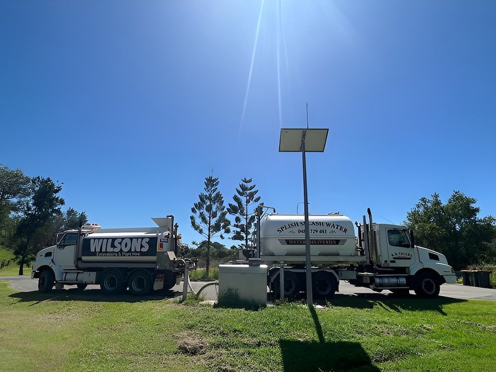 Two White Trucks Are Parked Next To Each Other In A Grassy Field — Wilsons Excavations & Plant Hire in Myocum, NSW