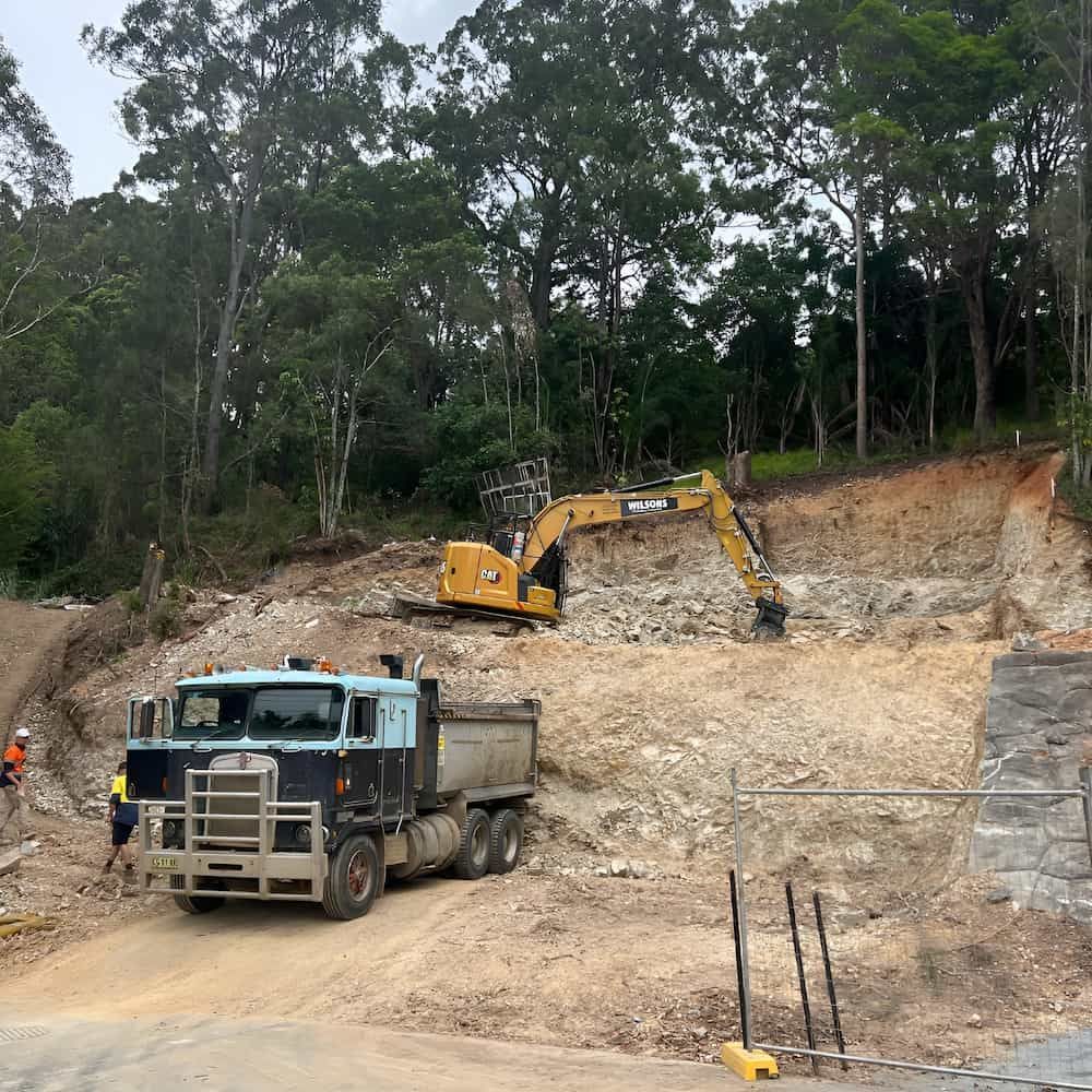 A Dump Truck Is Parked On A Dirt Road Next To An Excavator — Wilsons Excavations & Plant Hire in Bangalow, NSW
