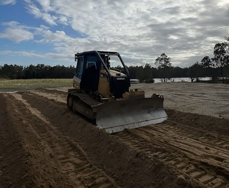 A Bulldozer Is Driving Through A Dirt Field — Wilsons Excavations & Plant Hire in Myocum, NSW
