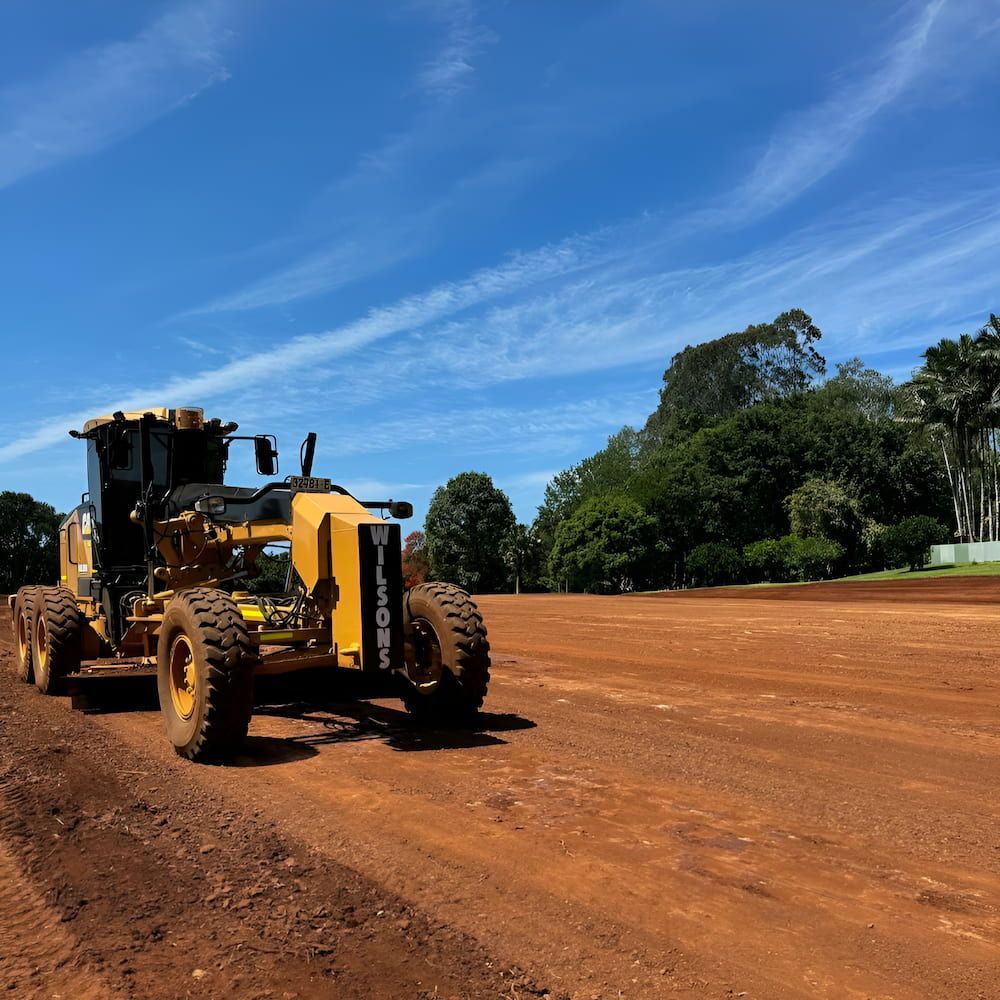 A Yellow Tractor Is Driving On A Dirt Road — Wilsons Excavations & Plant Hire in Myocum, NSW