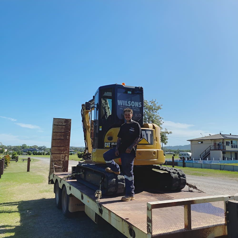 A Man Is Standing In Front Of A Bulldozer That Says Wilsons — Wilsons Excavations & Plant Hire in Byron Bay, NSW