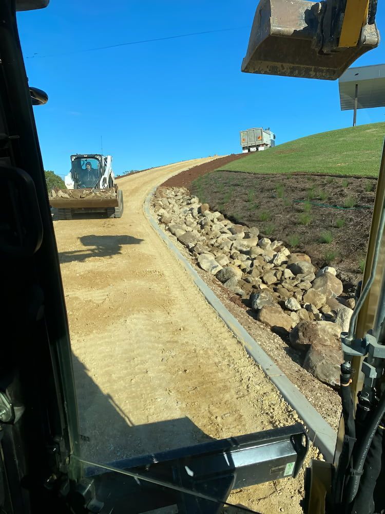 A Construction Vehicle Is Driving Down A Dirt Road — Wilsons Excavations & Plant Hire in Myocum, NSW