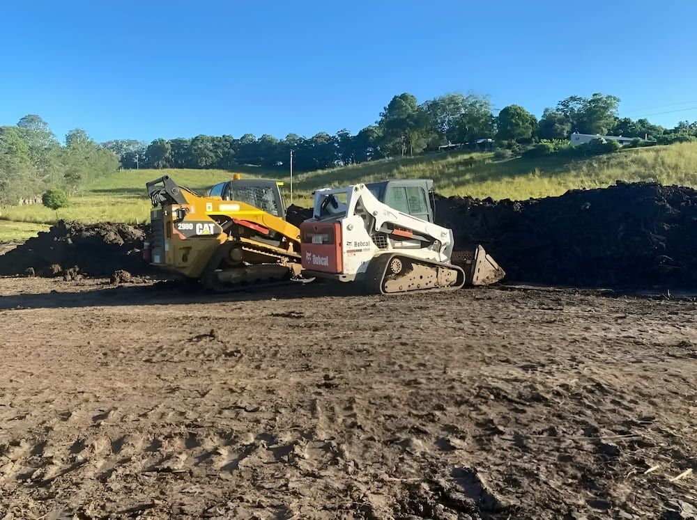 A Bulldozer And A Dumpster Are Sitting In A Dirt Field — Wilsons Excavations & Plant Hire in Myocum, NSW