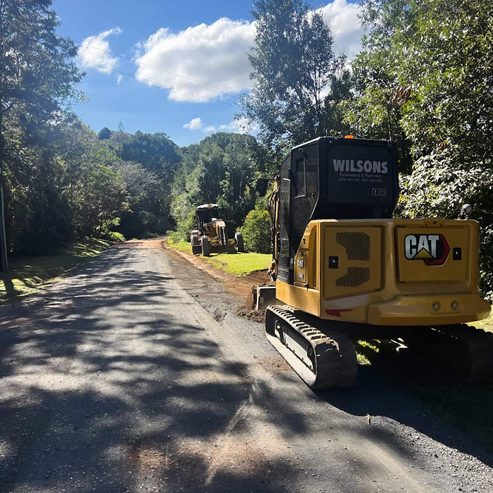 A Yellow Cat Excavator Is Parked On The Side Of A Road — Wilsons Excavations & Plant Hire in Myocum, NSW