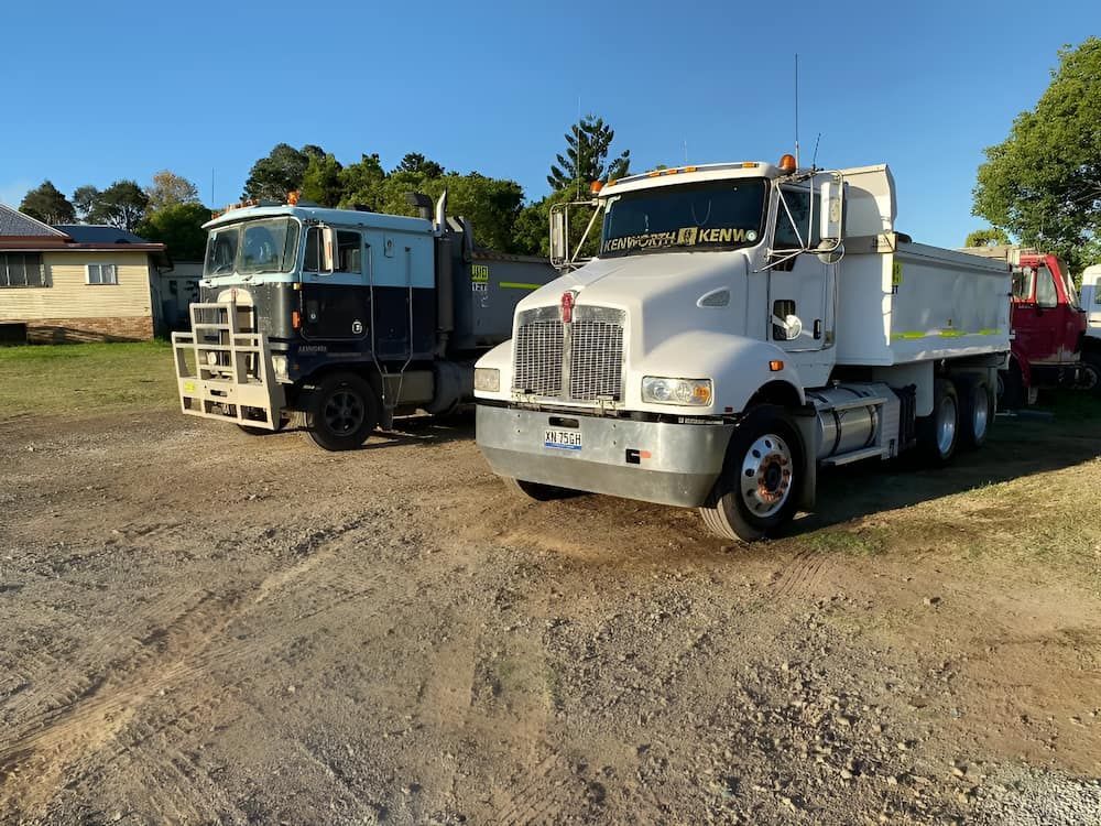 Two Dump Trucks Are Parked Next To Each Other In A Dirt Lot — Wilsons Excavations & Plant Hire in Myocum, NSW