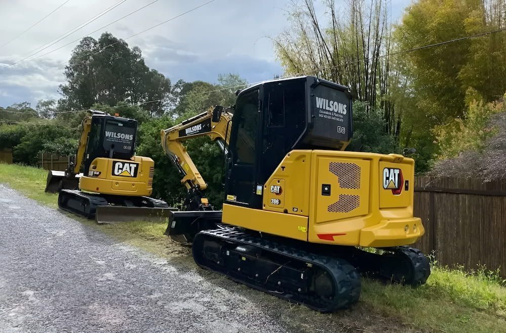 Two Cat Excavators Are Parked On The Side Of A Road — Wilsons Excavations & Plant Hire in Myocum, NSW