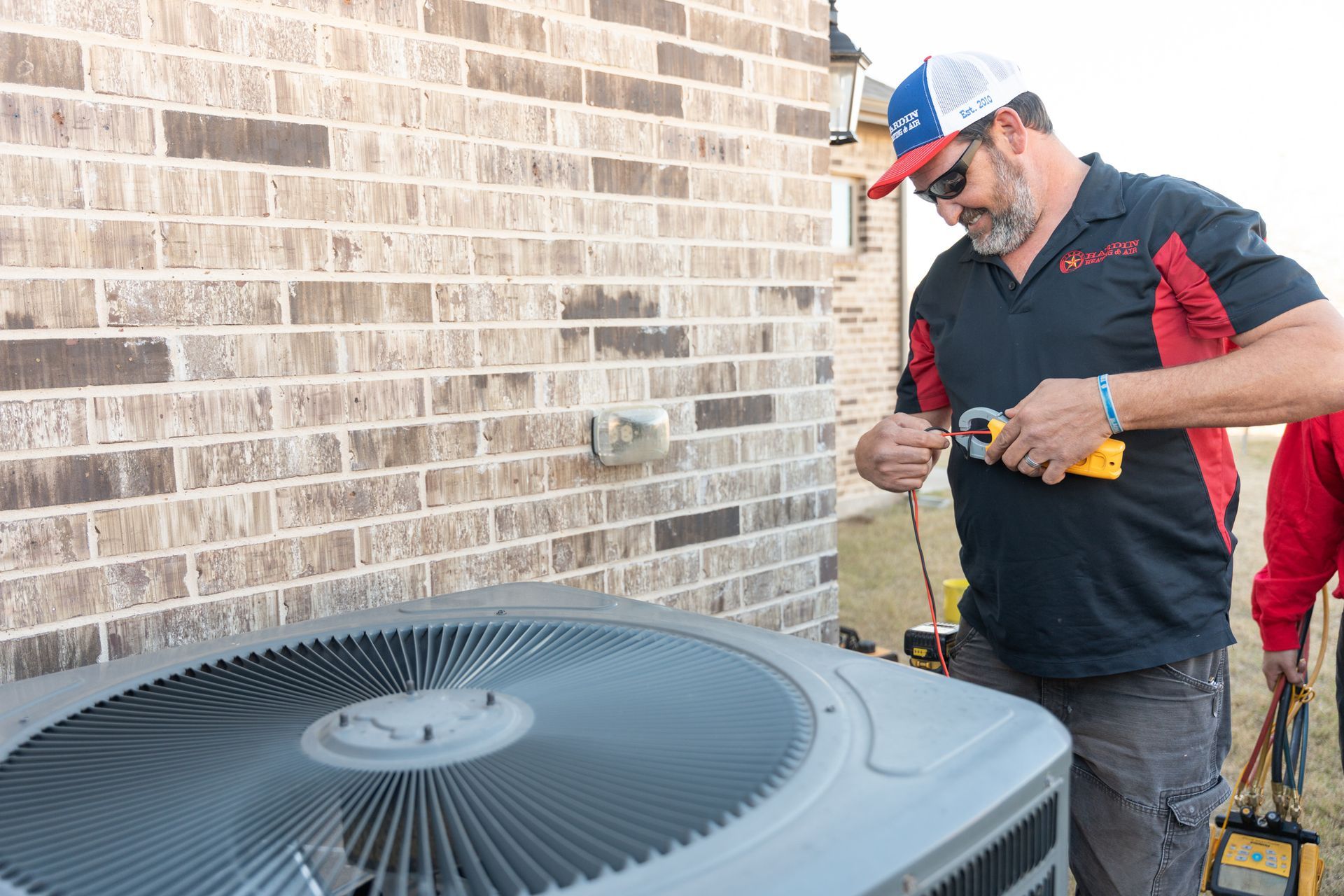 Hardin Heating & Air Technician working on an air conditioning unit outside a brick building.