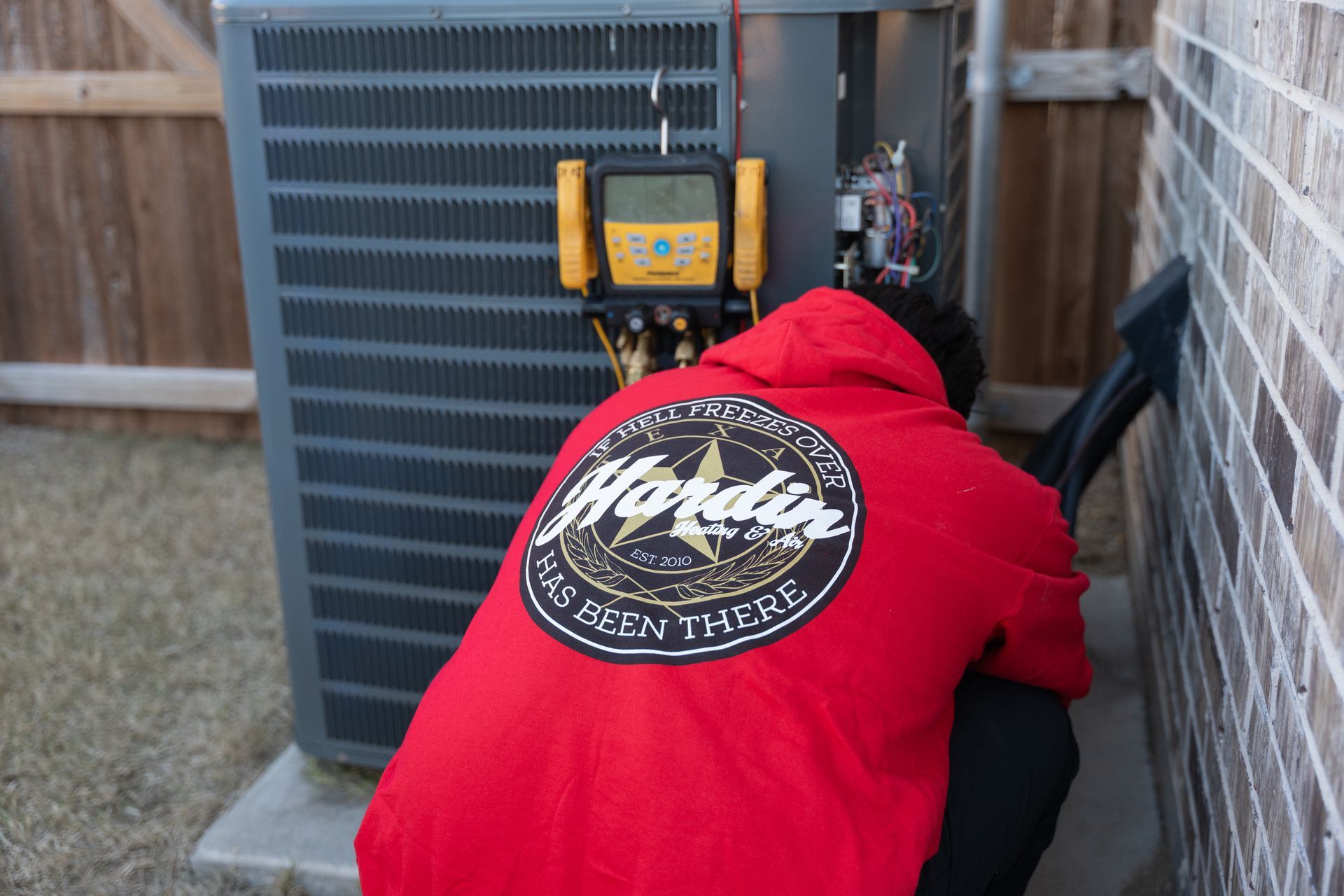 Person in red hoodie servicing an AC unit outside.