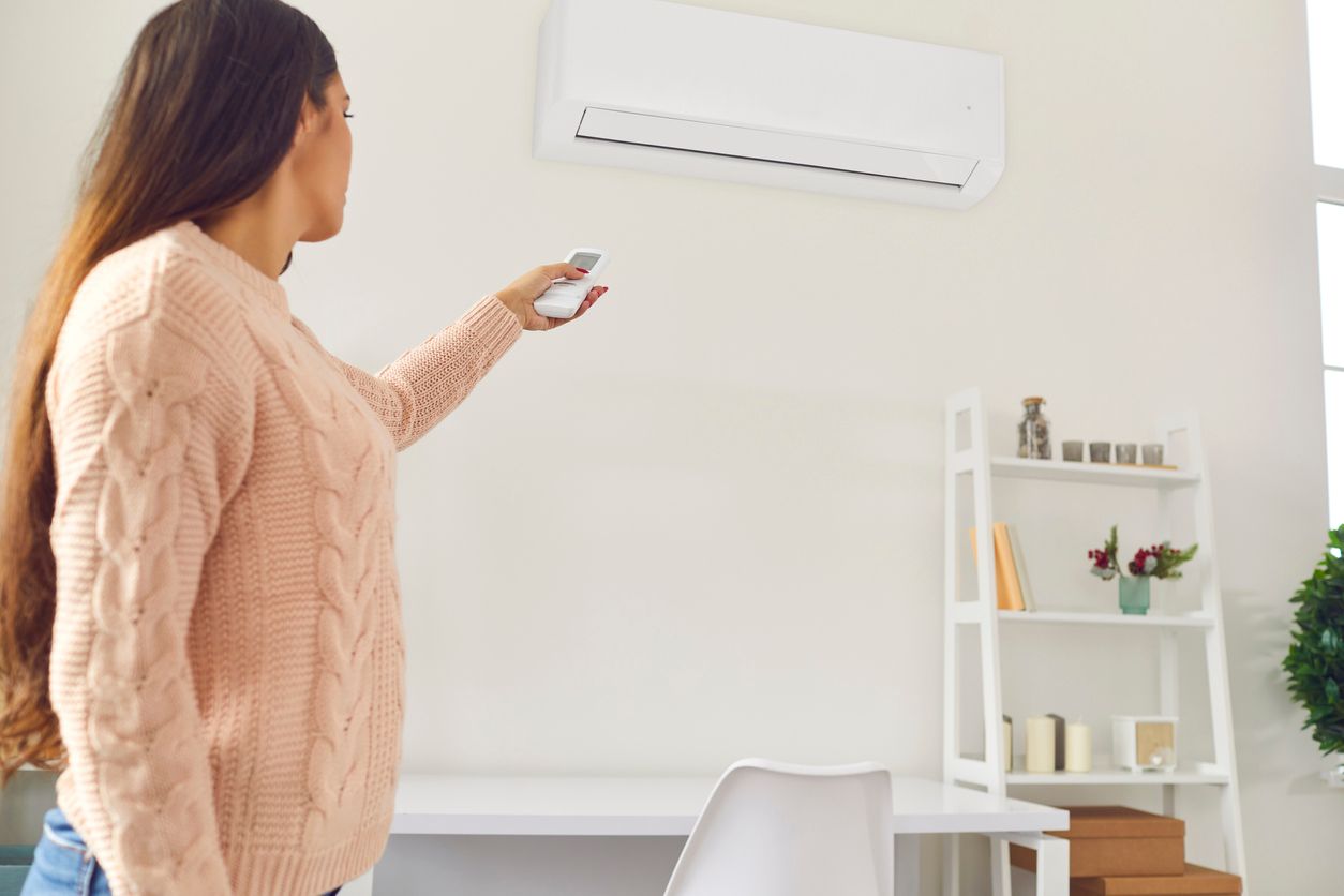 Woman using a remote to adjust a wall-mounted air conditioner in a bright room.