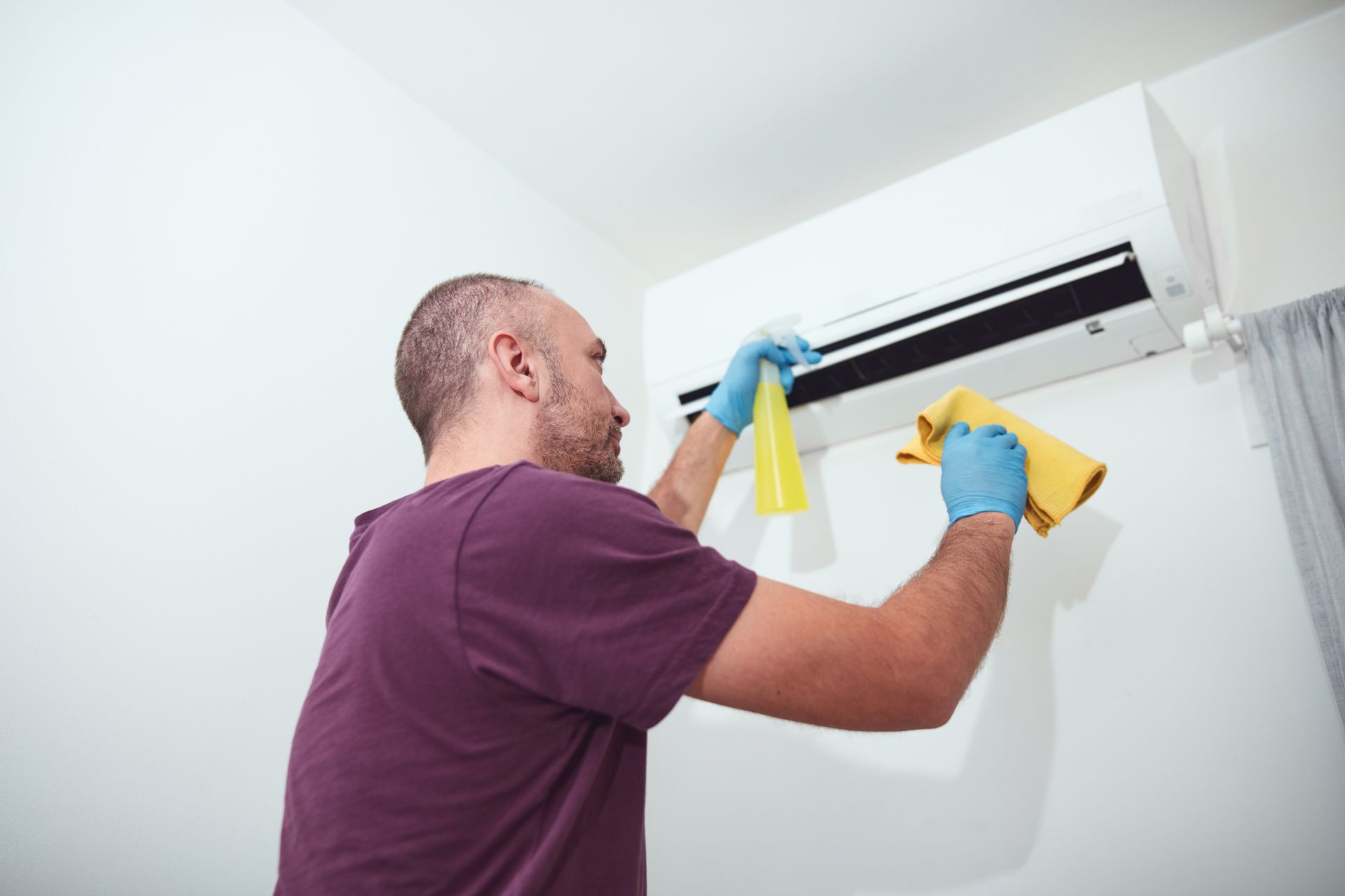 Homeowner cleaning and maintaining an outdoor air conditioning unit in Midlothian, Texas.