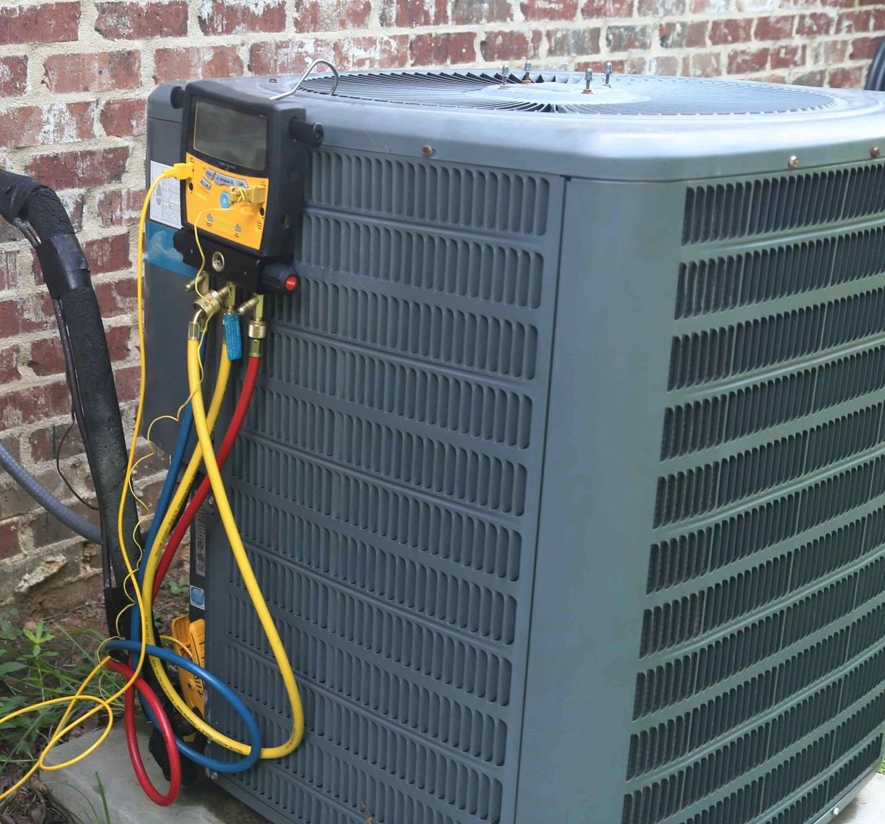 An air conditioner is being serviced by a brick wall