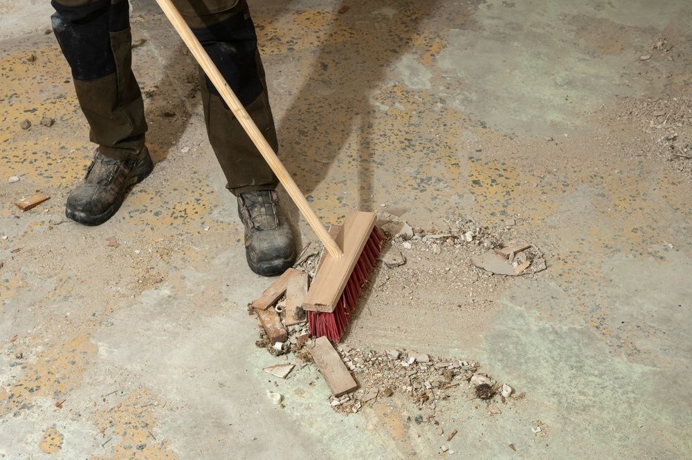 Worker sweeping dust and debris from a concrete floor with a broom.