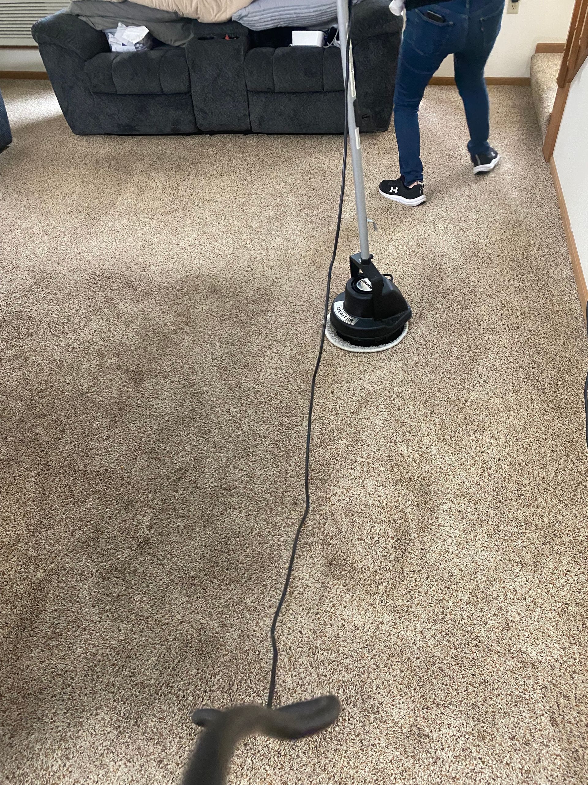 Vacuum cleaner on beige carpet with a person standing nearby in a living room