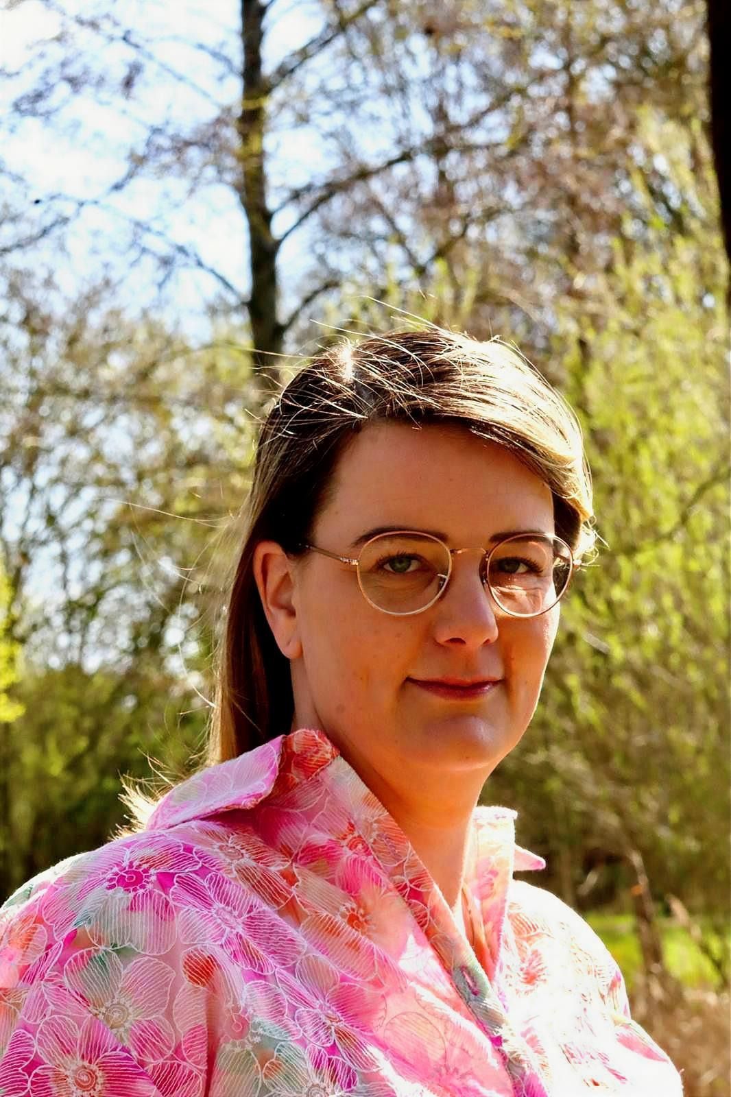 Een vrouw in een crèmekleurige blazer staat voor kale bomen.