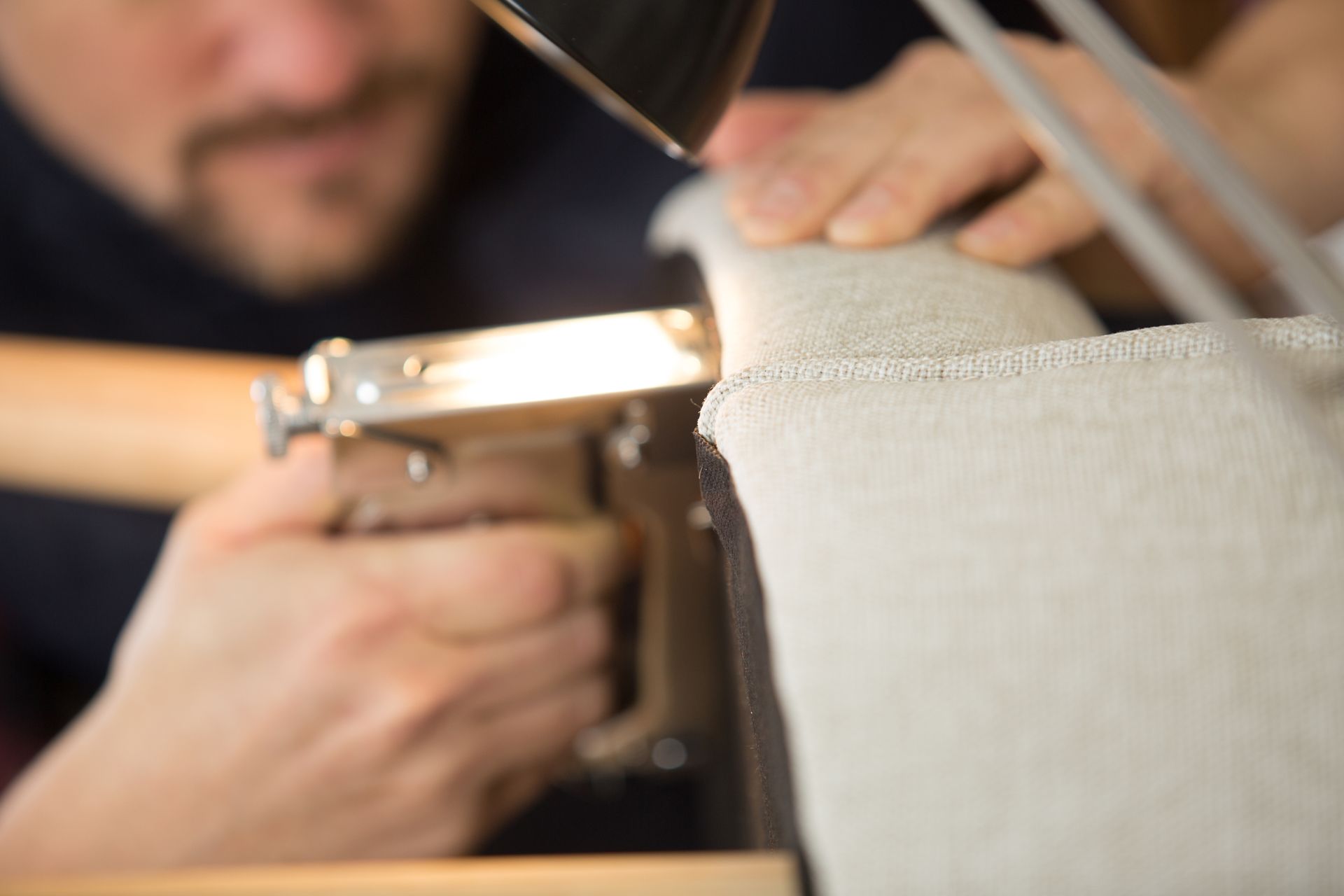 An upholstery restoration technician securing new fabric to a furniture frame.